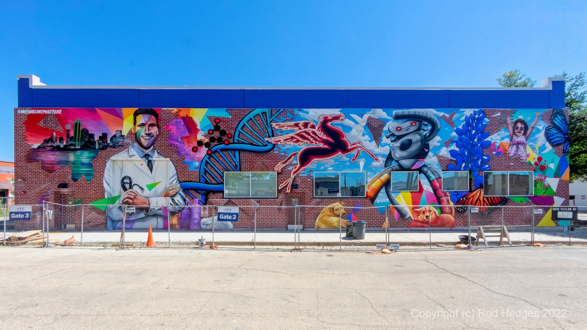 This colorful mural spans the entire side of a building and contains iconic symbols associated with Dallas, Texas. From left to right the images depict the Dallas skyline silhouetted against a bright orange sunset, a scientist wearing a lab coat, Pegasus, the Traveling Man, and a sprig of bluebonnets. Interspersed among these icons are images of 3 dogs, a child, butterflies and chemical molecules. 